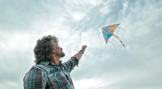 Handsome man flying colourful kite in the sky in spring.