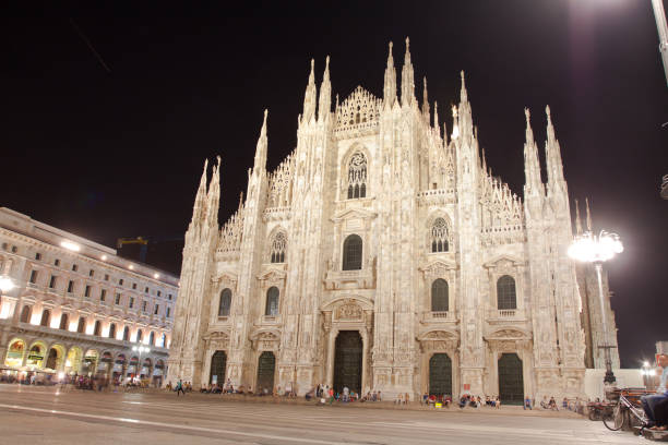 Cathedral Duomo di Milano at summer night. People are sitting in front of cathedral. At right side are sitting more people on square. Long exposure