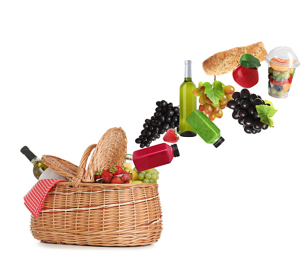 Different products falling in picnic basket on white background