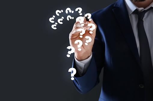 Businessman using virtual screen with question mark symbols on dark background, closeup