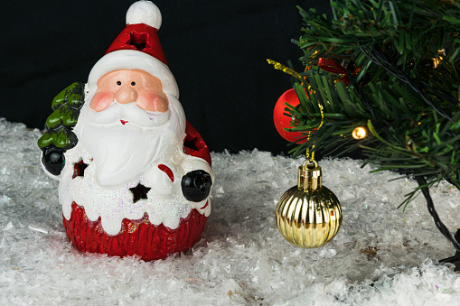 Table covered with snowflakes with Christmas decorations. Santa Claus, Christmas tree with red, gold balls and lights. Selective focus.