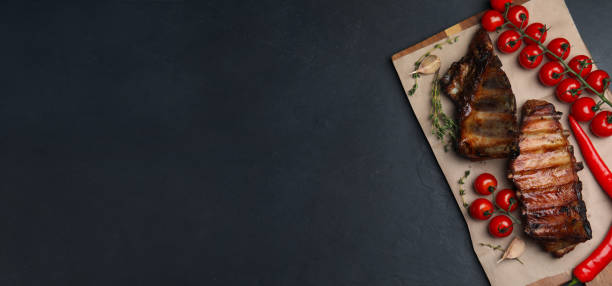 istock Serving board with tasty grilled ribs and space for text on black table, top view. Banner design 1345538423