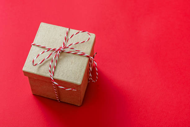 istock Christmas gift box on red color background. Red white striped string tied on brown kraft present. 1345538613