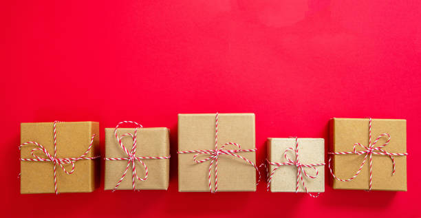 istock Christmas gift boxes on red color background. Red white striped string tied on brown kraft presents. 1345538676