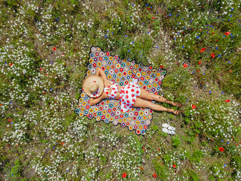 Relaxation. A woman lies in a field among daisies and poppies. Aerial view.