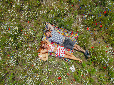 A man and a woman lie in a field among poppies and daisies. Aerial view.