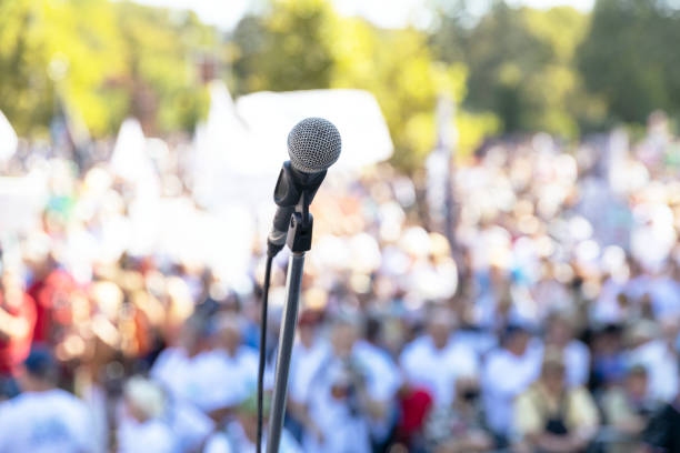 Protest or public demonstration, focus on microphone, blurred crowd of people in the background Focus on microphone, blurred group of people at mass protest or public demonstration in the background political rally stock pictures, royalty-free photos & images