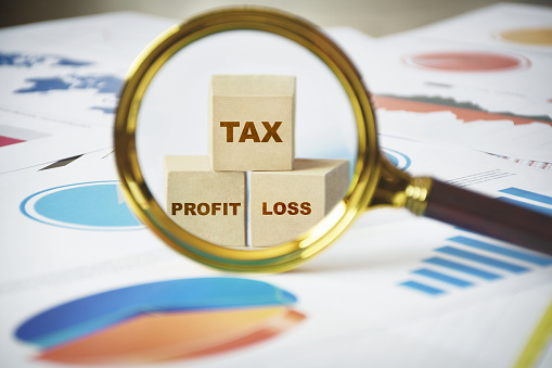 Tax concept. Profit and loss and tax statements. Magnifying glass focus on words tax, profit and loss. Tax season