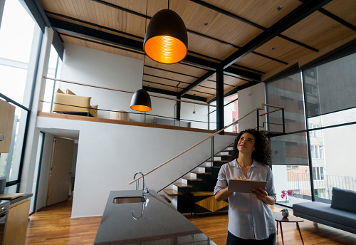 Latin American woman controlling the lights of her house using a home automation system - smart home concepts