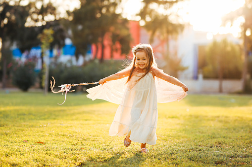 Little girl dressed in a fairy's outfit prances over the green grass holding a wand
