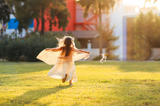Cute little girl dressed in a fairy outfit using a twig as a magic wand.