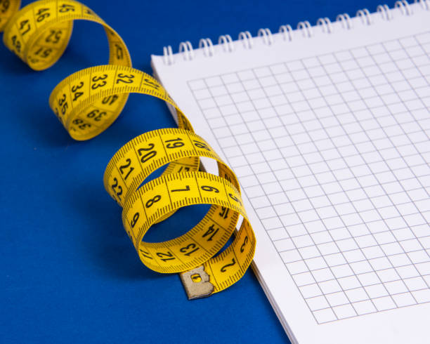istock Yellow spiral tape measure and notebook on dark blue background 1345549607