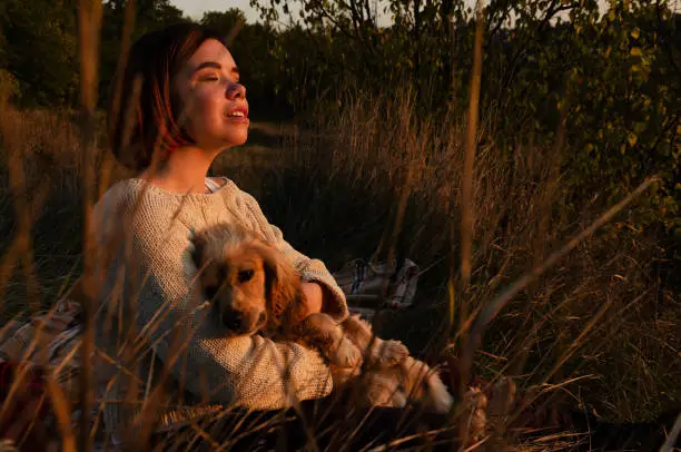 Photo of Thoughtful woman with short hair sitting on the ground during golden hour with her pet dog, enjoying sunset.