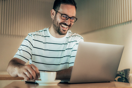 Portrait of young smiling cheerful entrepreneur in cafe while working with laptop