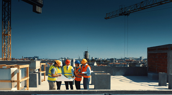 Closeup side view of group of building contractors and engineers walking on the top of the building under construction and discussing about some future plans.