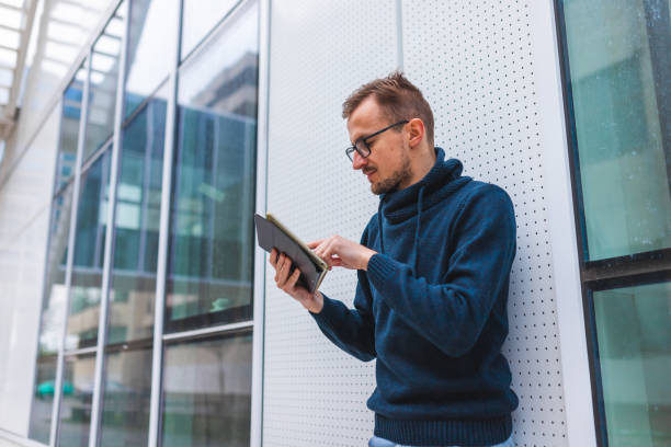 istock Young man with glasses using his digital tablet outside an airport with beautiful modern architecture 1345555842