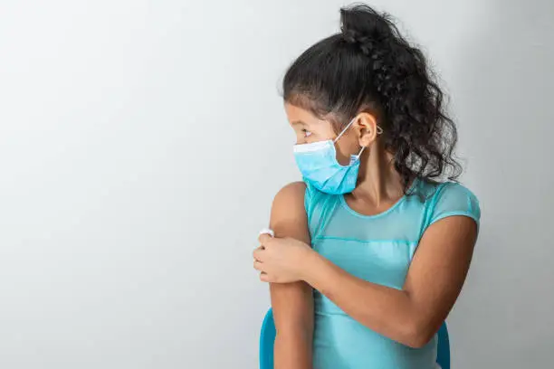 little girl looking to the right as she holds a cotton ball on her arm after injuring her skin or injecting covid-19 vaccine. First aid. Medical, pharmaceutical and sanitary concept.