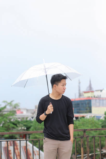 jóvenes de pie con un paraguas en un parque de la ciudad - umbrella men business businessman fotografías e imágenes de stock