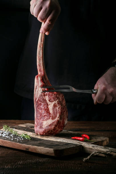 istock The chef's hands hold a raw Tomahawk a beef steak and a meat fork over a chopping Board 1345557889