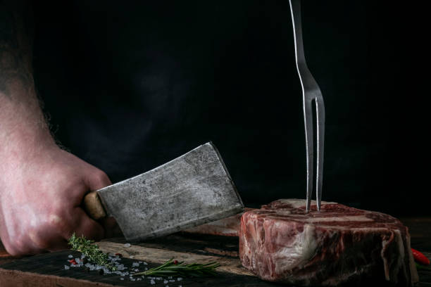 istock A butcher cuts beef Tomahawk steak on a bone with a cleaver on a wooden cutting Board on a dark background 1345557898