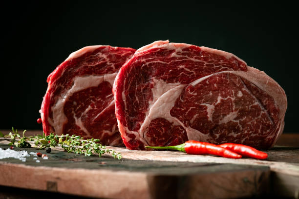 Raw rib eye beef steak with pepper and herbs on a wooden background in a butcher shop Raw rib eye beef steak with pepper and herbs on a wooden background in a butcher shop rib eye steak stock pictures, royalty-free photos & images