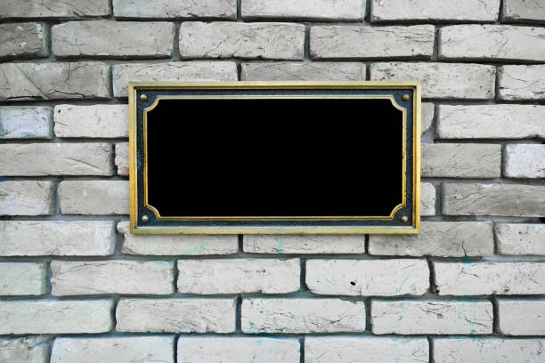 Black commemorative plaque in golden frame fixed on white brick wall stock photo