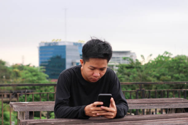 istock Asian Men sitting enjoying using phone in a city park 1345560950