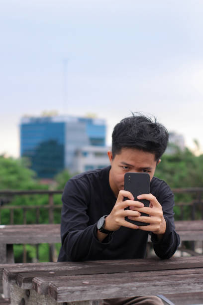 istock Asian Men sitting enjoying using phone in a city park 1345561062