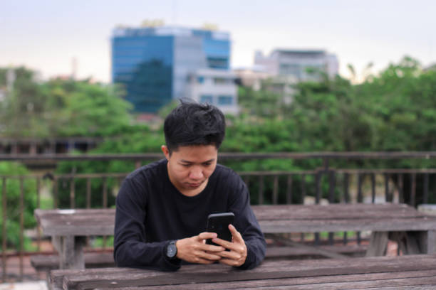 istock Asian Men sitting enjoying using phone in a city park 1345561083