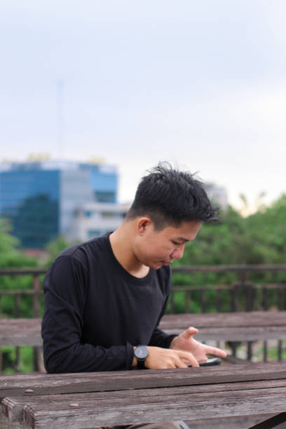 istock Asian Men sitting enjoying using phone in a city park 1345561137