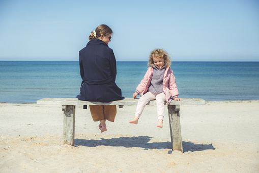 Mother and cute little danish girl relaxing on beach bench and enjoying the perfect ocean view