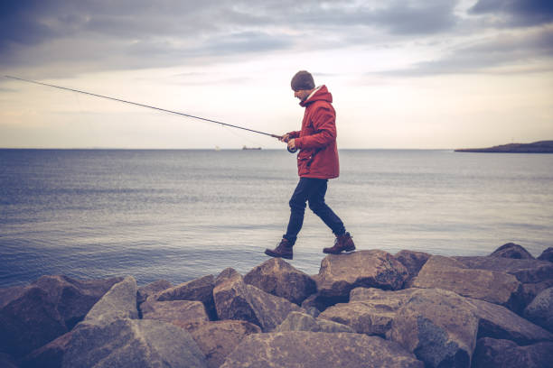 Saltwater Fly-fishing from a rocky pier in the capital city Copenhagen, Denmark during autumn, winter or fall.  Male angler wearing fashionable red  jacket and knit hat.