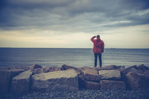 Saltwater Fly-fishing from a rocky pier in the capital city Copenhagen, Denmark during autumn, winter or fall.  Male angler wearing fashionable red  jacket and knit hat.