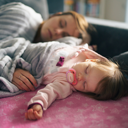 Small caucasian baby sleeping on the sofa bed with her mother at home in day single mother tired family parenthood and motherhood care and bonding concept