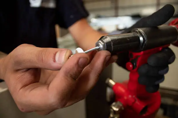 The worker uses a rivet hand gun, and inserts a rivet into it. Manual rivet wrench.