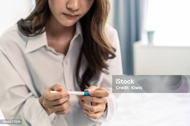 Close Up Of Woman Feeling Shock After Look At Positive Pregnancy Test Disappointed Attractive Beautiful Unplanned Pregnancy Girl Sit On Bed With Upset And Sad Face For Problem Dont Want To Pregnant Stock Photo - Download Image Now