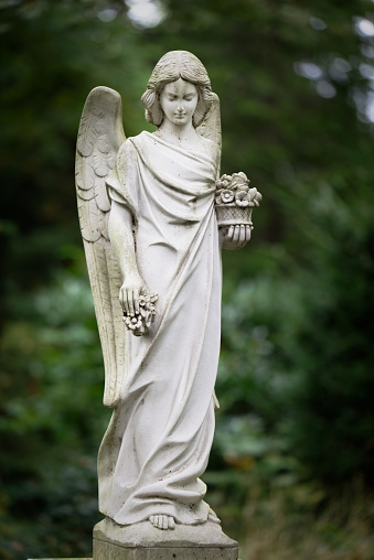 white angel with flowers in hand in front of blurred green background on a cemetery