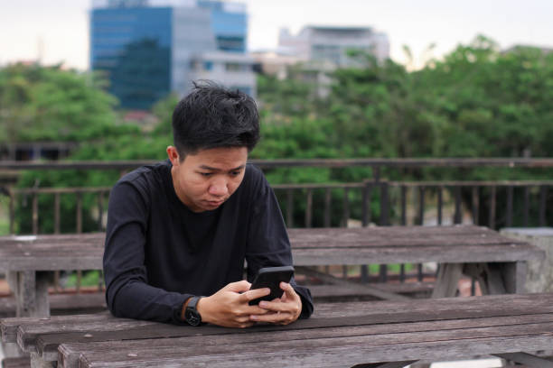 istock Asian Men sitting enjoying using phone in a city park 1345589318