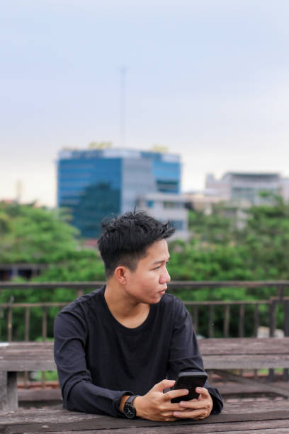 istock Asian Men sitting enjoying using phone in a city park 1345589325