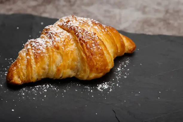 Fresh croissant with icing on black slate background