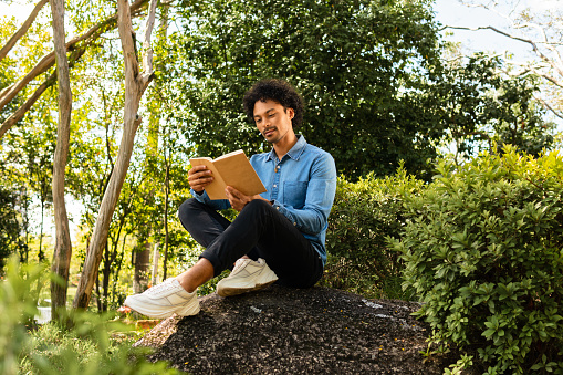 african american man reading book for leisure on top of rock