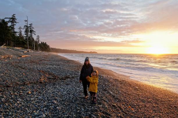 A mother and daughter posing for a photo on agate beach with the waves crashing to shore and the sun setting stock photo