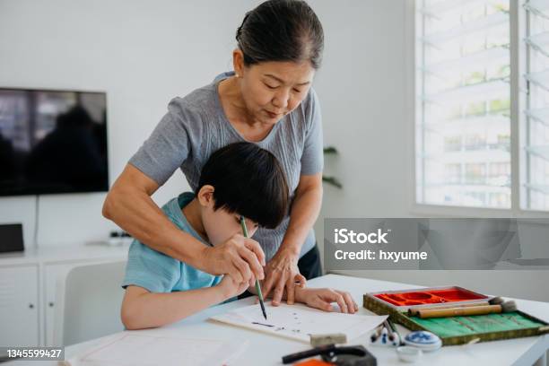 Senior Asian Woman Teaching Her Grandson Chinese Calligraphy At Home Stock Photo - Download Image Now