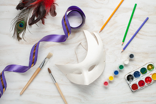 Paper Carnival mask and paints DIY on a white wooden background. Mardi Gras concept. Top view