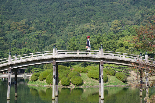 Beautiful Asia Woman Walking on a Wooden Arched Footbridge in the Garden / Park Enjoying Summer Scenics.