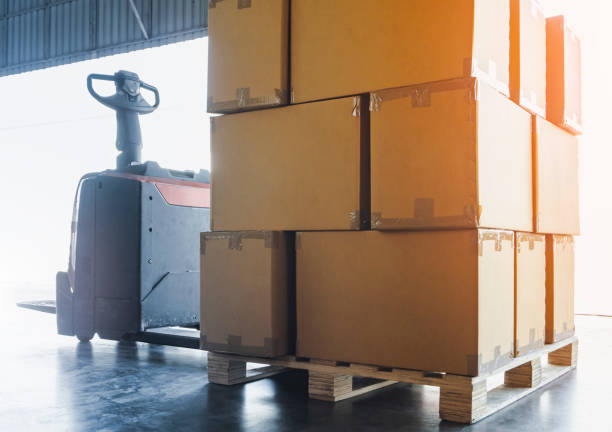 istock Package Boxes on Pallet with Electric Forklift Pallet Jack. Cargo Shipment Boxes Warehouse Logistics and Transportation. 1345610003