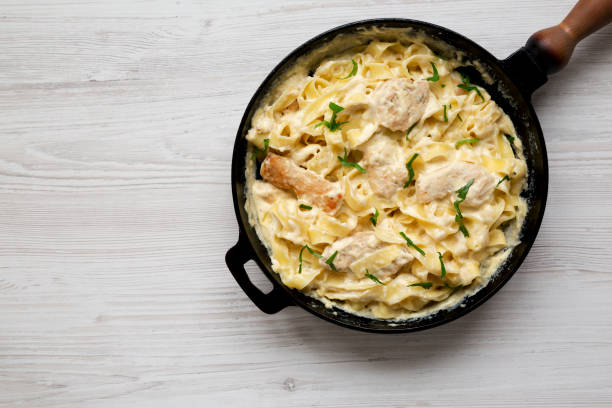 pollo casero fettuccine alfredo en una sartén de hierro fundido sobre un fondo de madera blanca, vista superior. lay plano, vista superior, desde arriba. espacio para texto. - noodles pasta chicken breast color image fotografías e imágenes de stock