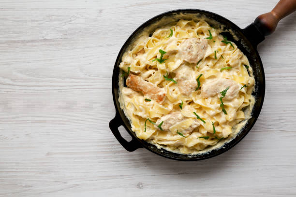 Homemade Chicken Fettuccine Alfredo in a cast-iron pan on a white wooden background, overhead view. Flat lay, top view, from above. Space for text. Homemade Chicken Fettuccine Alfredo in a cast-iron pan on a white wooden background, overhead view. Flat lay, top view, from above. Space for text. Fettuccine Alfredo stock pictures, royalty-free photos & images