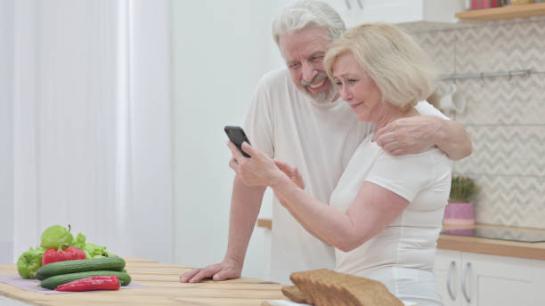 istock Old Couple Browsing internet on Smartphone in Kitchen 1345615057