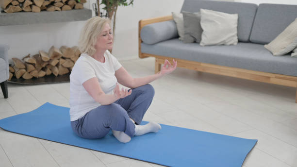 istock Peaceful Old Woman Meditating on Excercise Mat at Home 1345616159